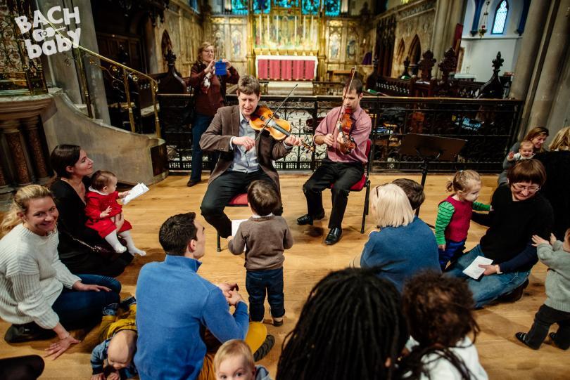 families and young children gather around two violinists