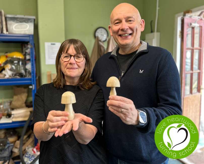 Husband and wife each holding a wooden mushroom.