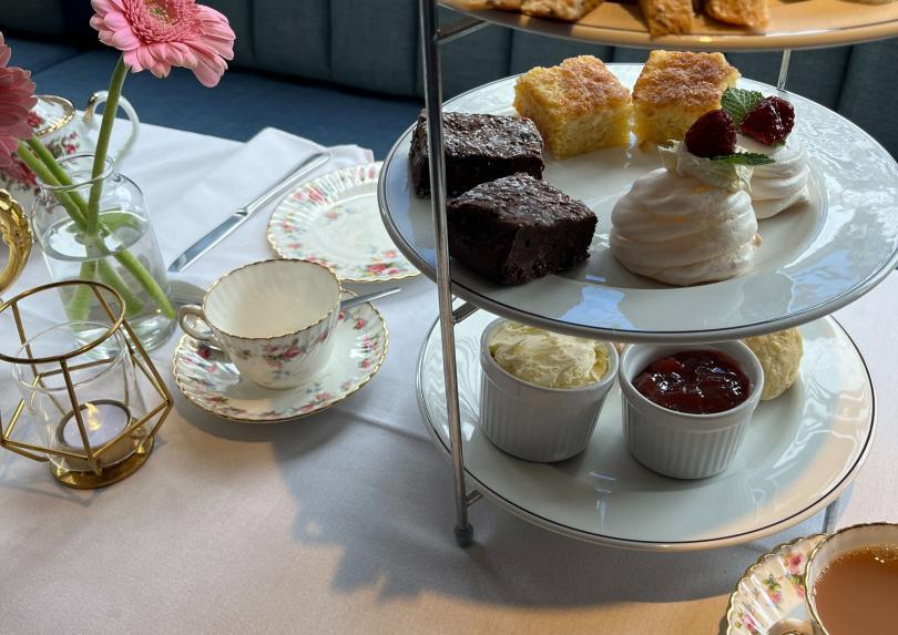 Metal table stand with various sandwiches and cakes, a vintage tea cup and a vase with a pink flower