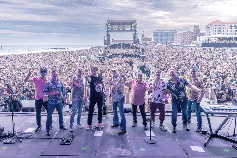 the beach boys band standing in a line on-stage. A massive crowd can be seen behind them.