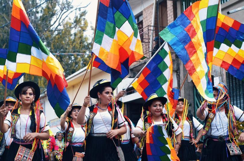 bolivan dancers in black and white outfits, raising colourful flags