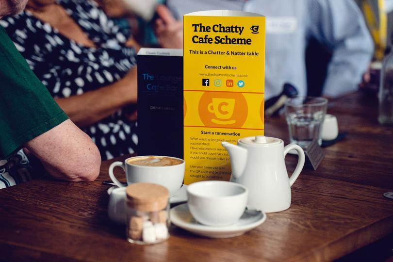 Image of a Chatty Cafe table flyer on a table with coffees