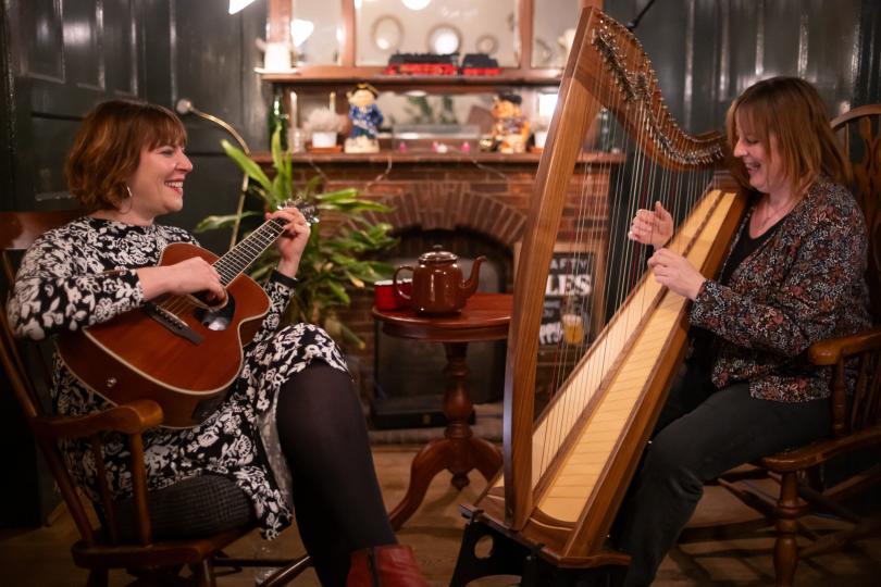 Photo shows two women playing music together on a guitar and a harp