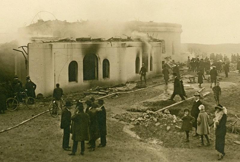 Sepia image of a burnt building with a small group of people stood in the foreground.