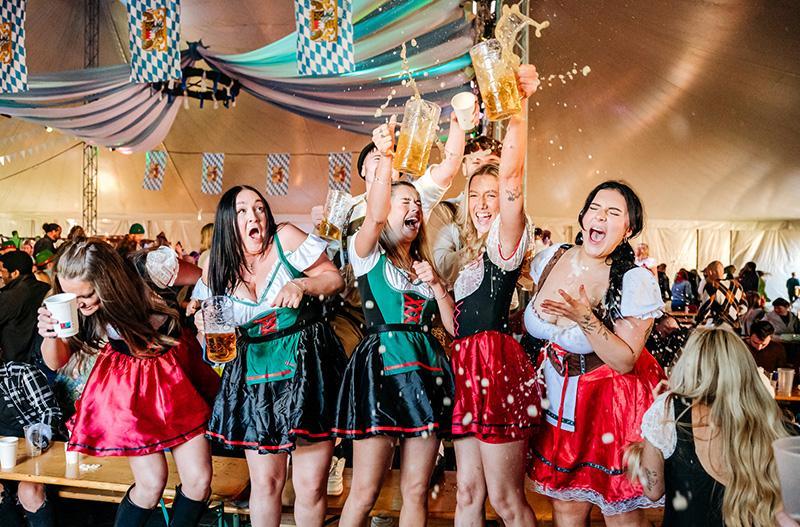 Women in traditional Bavarian fancy dress outfits drinking beer and clinking glasses