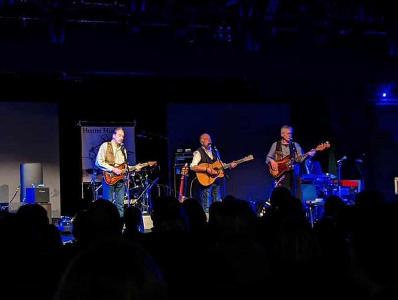 Photo of the trio Hunter Muskett on stage singing and playing guitars
