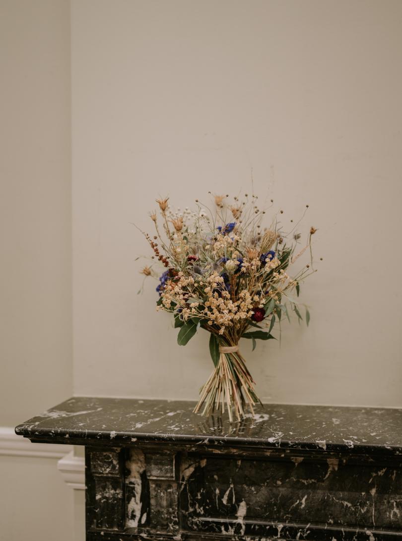 Beautiful bouquet of dried flowers standing up on black marble mantlepiece against white wall.