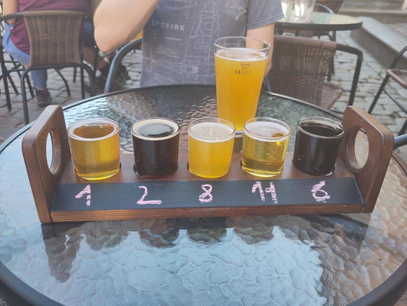 A flight of 5 different beers and a pint in the background