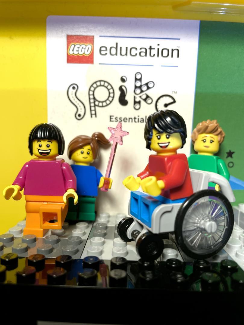 Image of poster saying ' LEGO Education Spike Essential' with four LEGO figures ranges in front of , one in a wheelechair