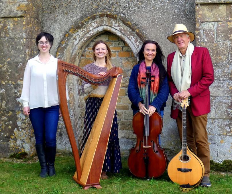 Photo of the four members of Moonrakers with musical instruments. They are standing in front of an old building with an arched doorway, like a church.