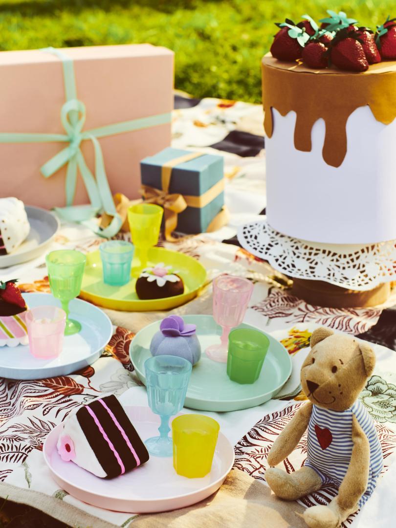 A picnic blanket propped with food and toys including an IKEA bear