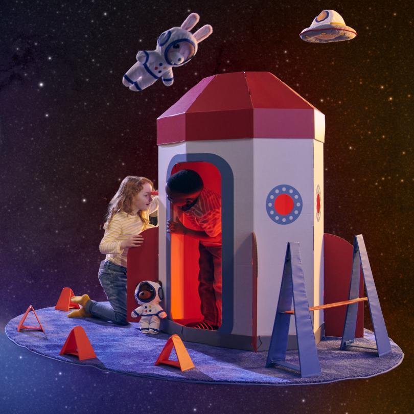 Children playing in a cardboard rocket in space