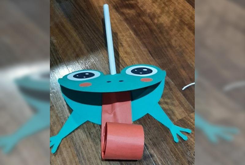 Photograph of a green cardboard fly catching frog with a pink tongue