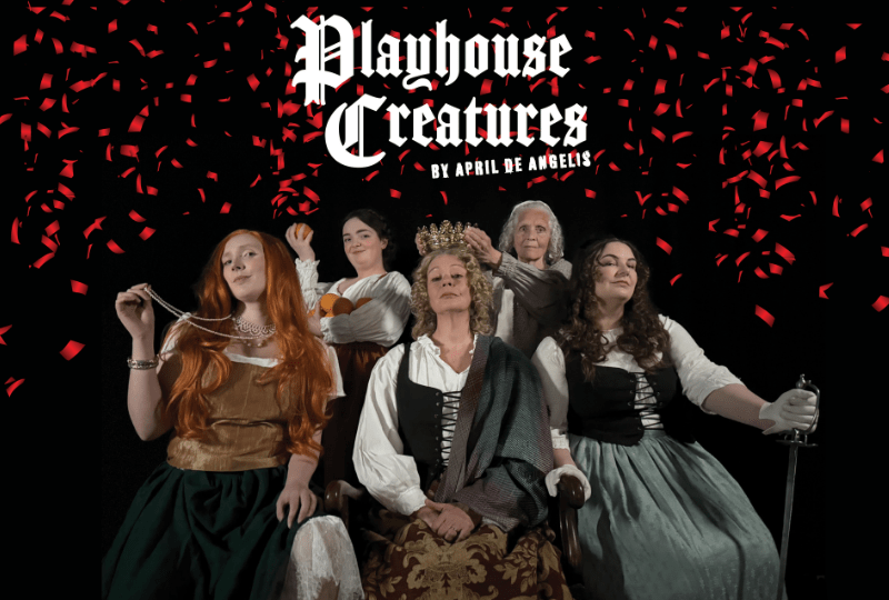 Photo of five women seated together, dressed as characters from the play in 1600s era clothing. Red confetti falls from above, and white text reads 'Playhouse Creatures by April de Angelis'.