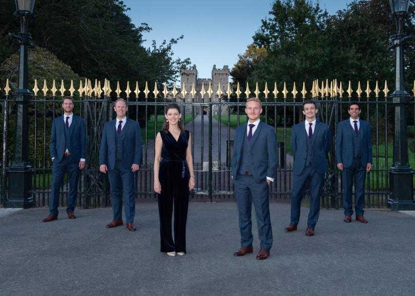 Queen's Six members standing in front of wrought iron gates