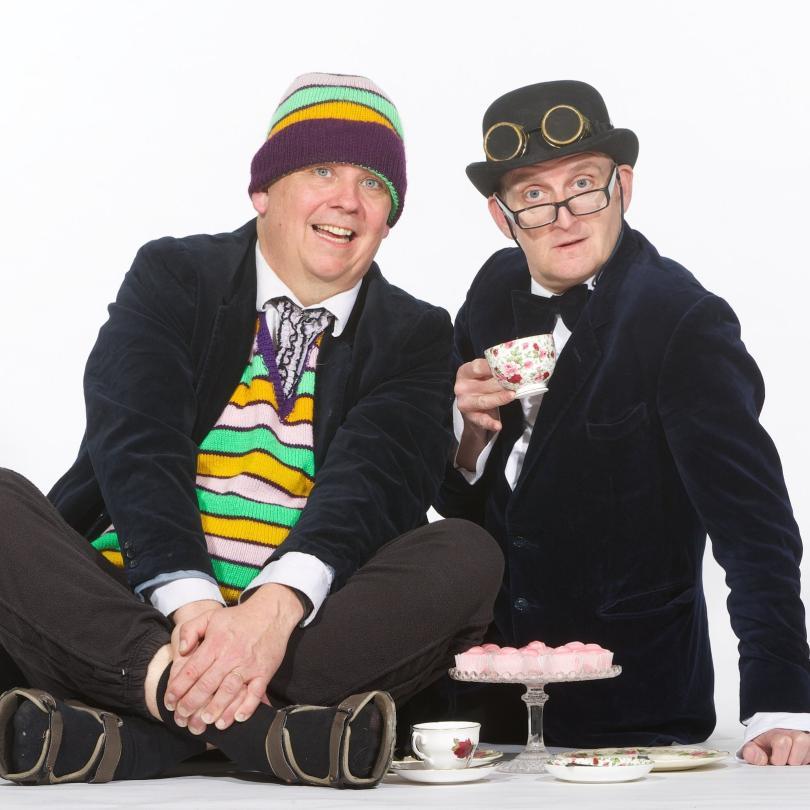 The Raymond and Mr Timpkins Revue dressed in black suits and hats and sitting on the floor - at Just The Tonic Reading