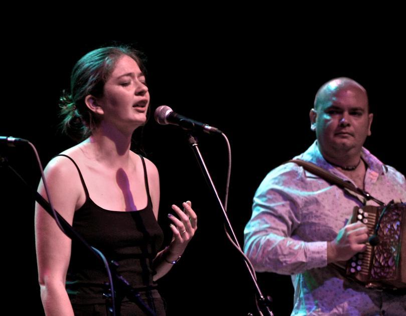 Photo of Jess and Rich Arrowsmith on stage. Jess is singing and Rich is playing a melodeon.