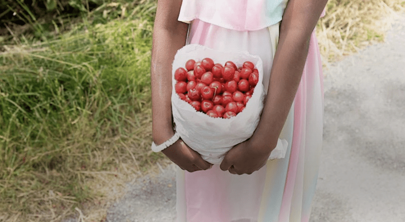 arms holding a bag of cherries with views of a garden behind