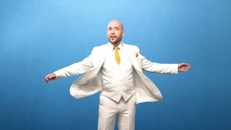 Tom Allen in a white suit in front of a blue backdrop