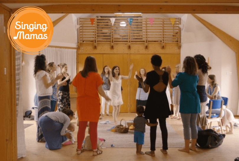 Singing Mamas logo and photo of a group of women standing in a circle and singing together
