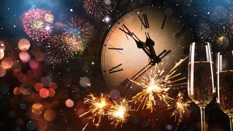 The image is a graphic of a clock face showing five to midnight. There are two glasses of champagne in the corner and fireworks across the whole illustration.