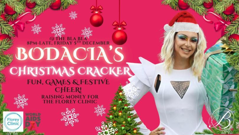 drag queen in a white outfit and Christmas hat on a pink background