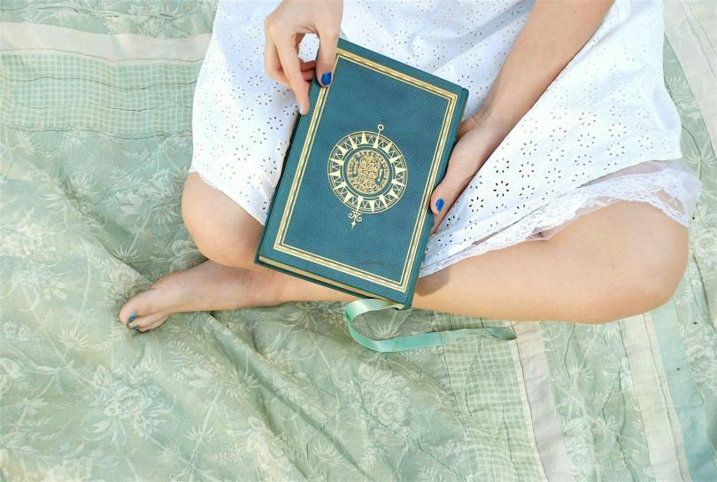 A woman sitting crosslegged with a book on her lap. But we only see her legs and the book.