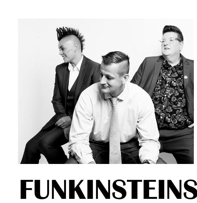 Black & White image of three seated white-skinned musicians looking to the left side. Person sat in front is wearing a white shirt and pale coloured tie, he has short hair and an amused expression; the person behind and to the left is wearing a dark satin effect suit and waistcoat and has dark spiked hair; the person behind and to the right is wearing a mid gray suit jacket and trousers with dark paisley shirt and glasses