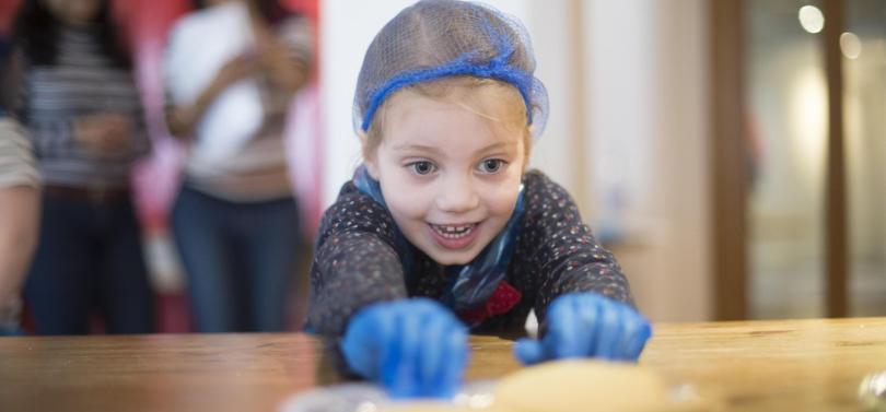 a young girl in a hairnet is rolling pastry