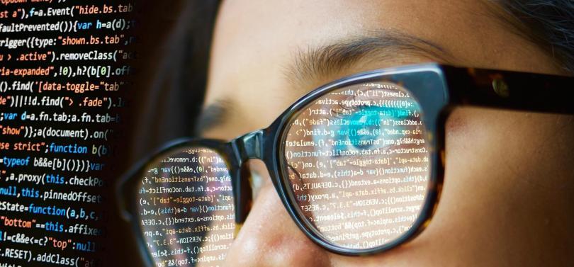 close-up of a girl wearing glasses with computer code reflected in them