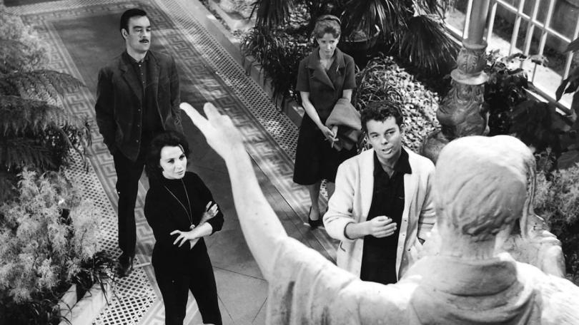 Four people standing in a garden looking up at a statue