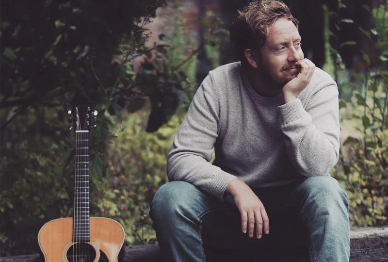 photo of singer James Krby in a grey jumper next to his guitar at Village Concerts in Purley-On-Thames