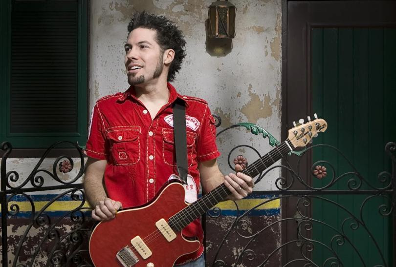 A man in a red shirt, holding a red guitar