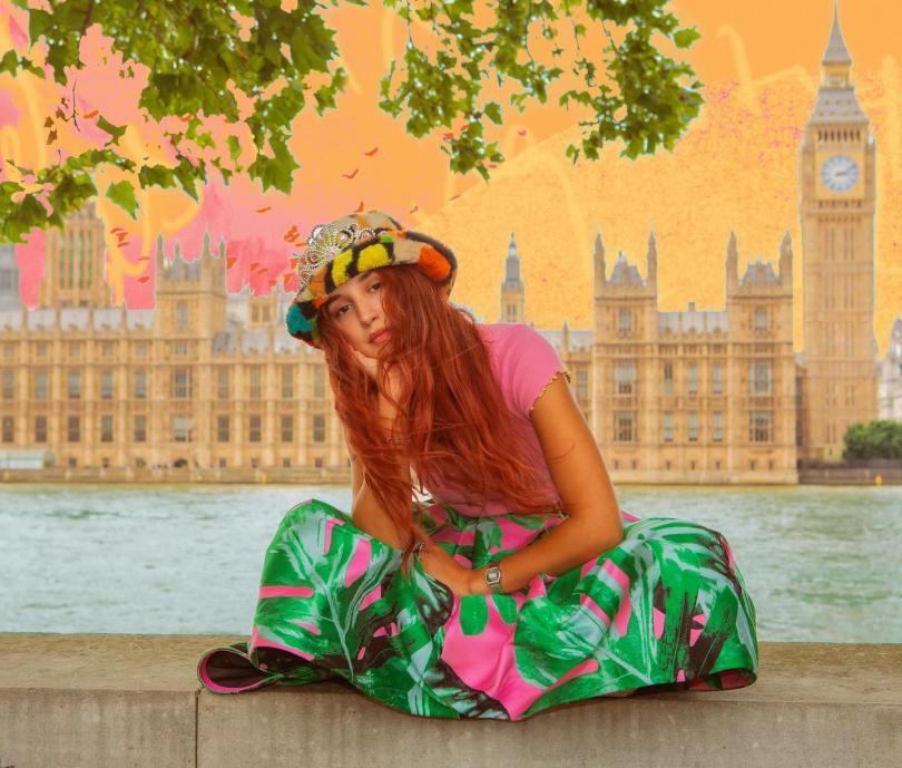 Singer Rubberband Girl with long red hair, sitting cross-legged in front of the Houses of Parliament