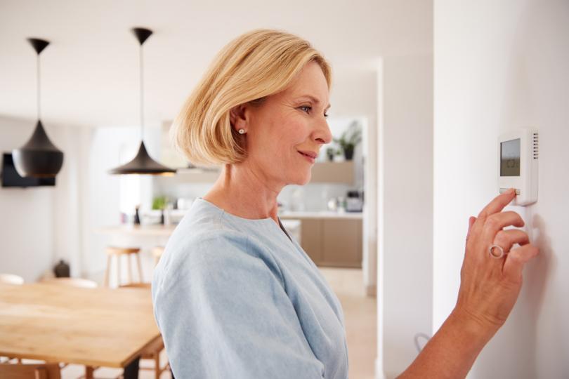 A woman adjusting a room thermostat