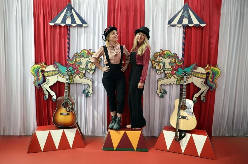 Sounds of the Sirens - two women in dungarees stnading on circus-style rostra next to their guitars