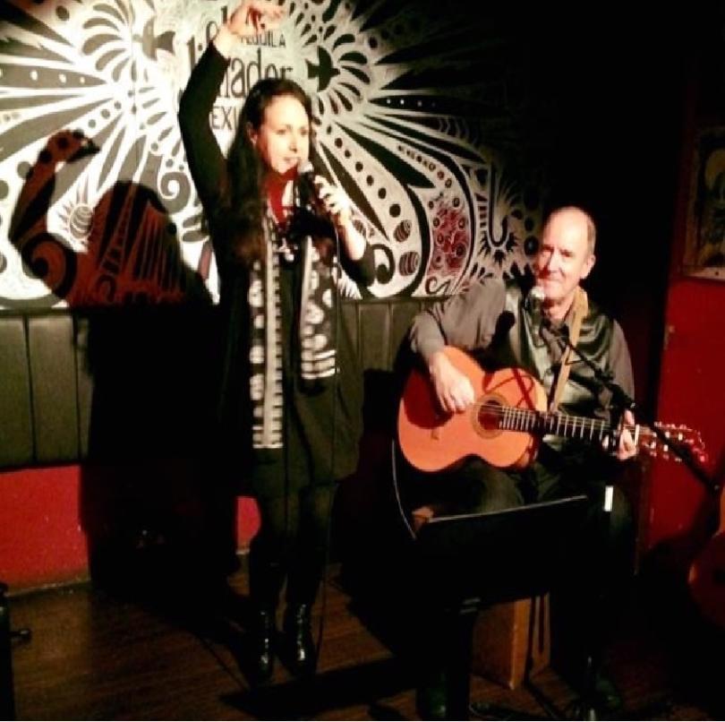 Photo of Skinner and T'witch on stage. In the photo Sandra Twitchett is singing, with her arm raised above her head and Steve Skinner is playing guitar.