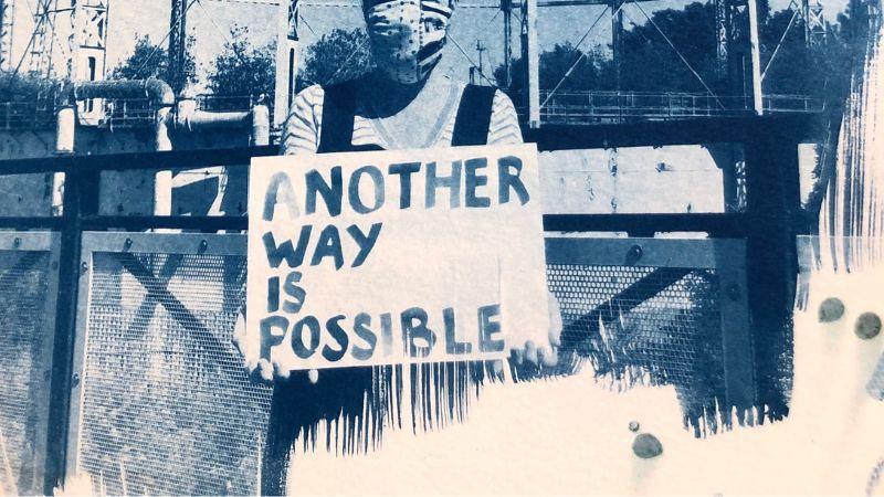 blue print of a woman holding a banner saying another way is possible