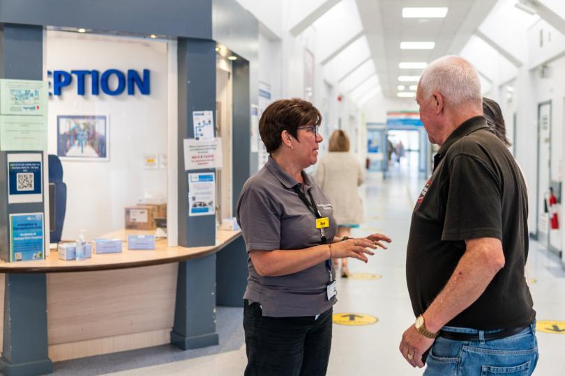 A volunteer speaking to a visitor in a hospital reception area