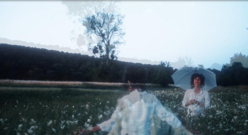 Video still featuring several superimposed images of a curly-haried woman in a field