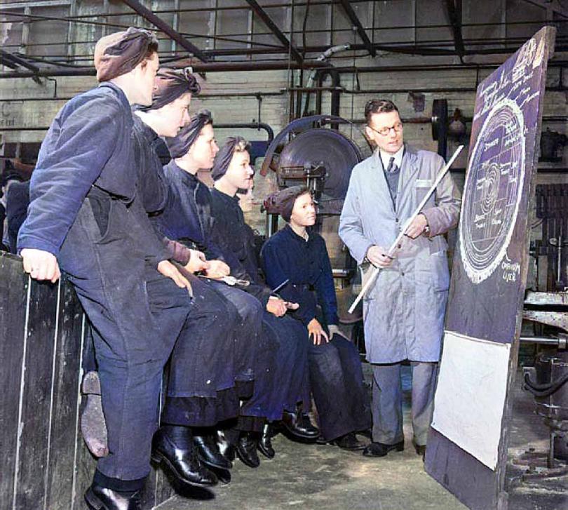 women in overalls limed up watching an instructor during the war