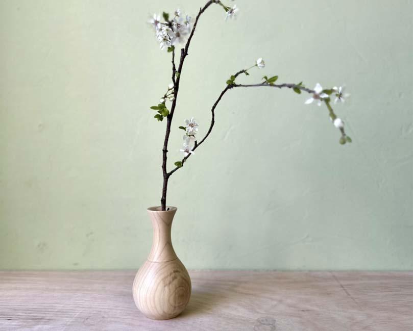 A wooden bud vase containing a sprig of cherry blossom.