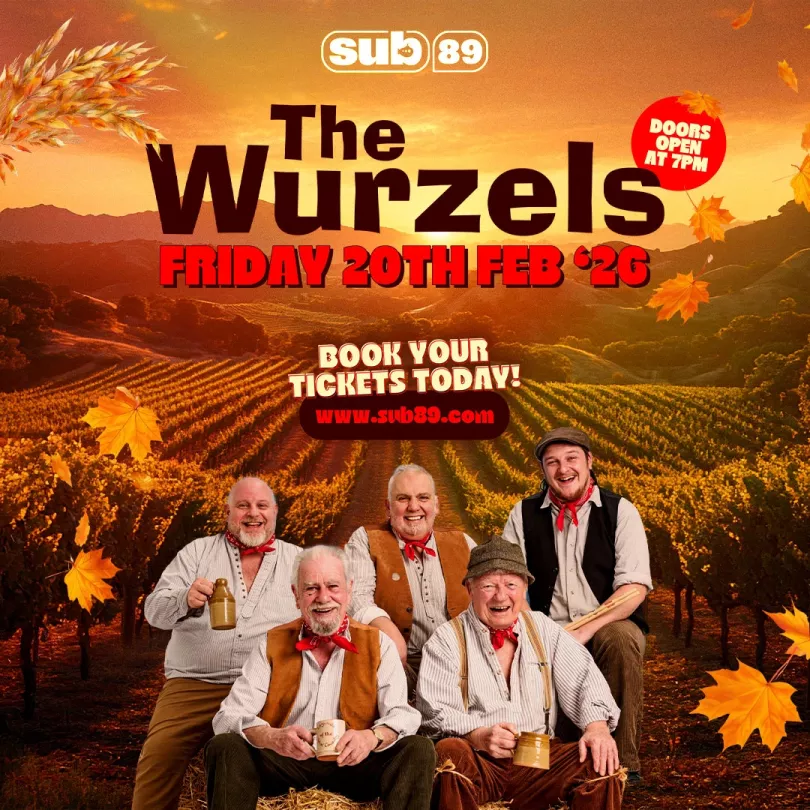The Wurzels wearing country clothes and standing by a fence