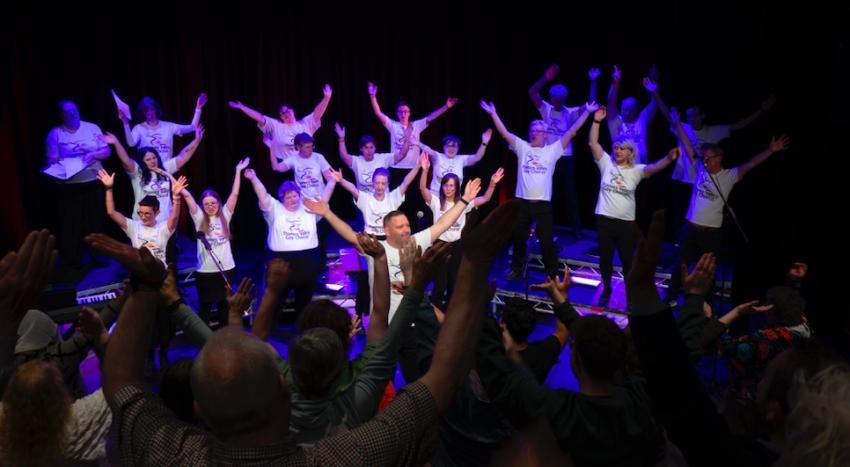 Performance photo of the choir with their hands in the air