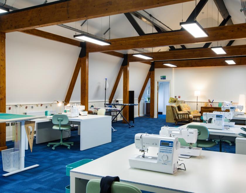 A sewing room with several workstations, cutting tables, and professional irons