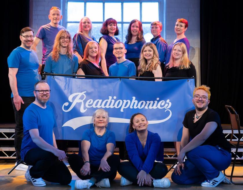 A cappella singing group all wearing blue, posed around a sign saying "Readiophonics"