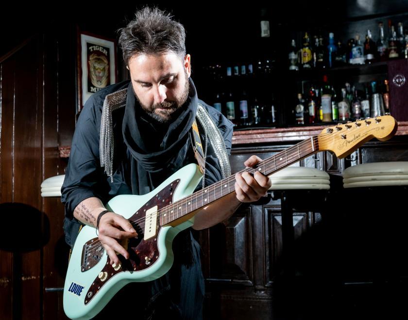 Photo of a performer wearing dark clothing and playing an electric guitar, in a bar room decorated black and white