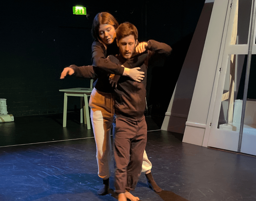 The Dark rehearsal image 2 - 2 performers rehearsing, one is standing behind the other reaching their arms around their torso