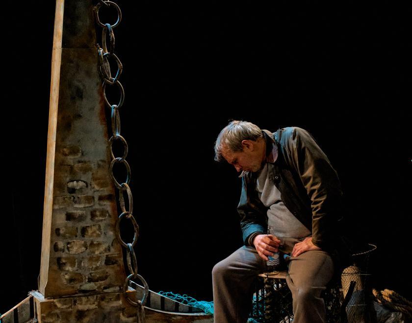 A performer sits on a lobster trap, slumped over and looking dejected.