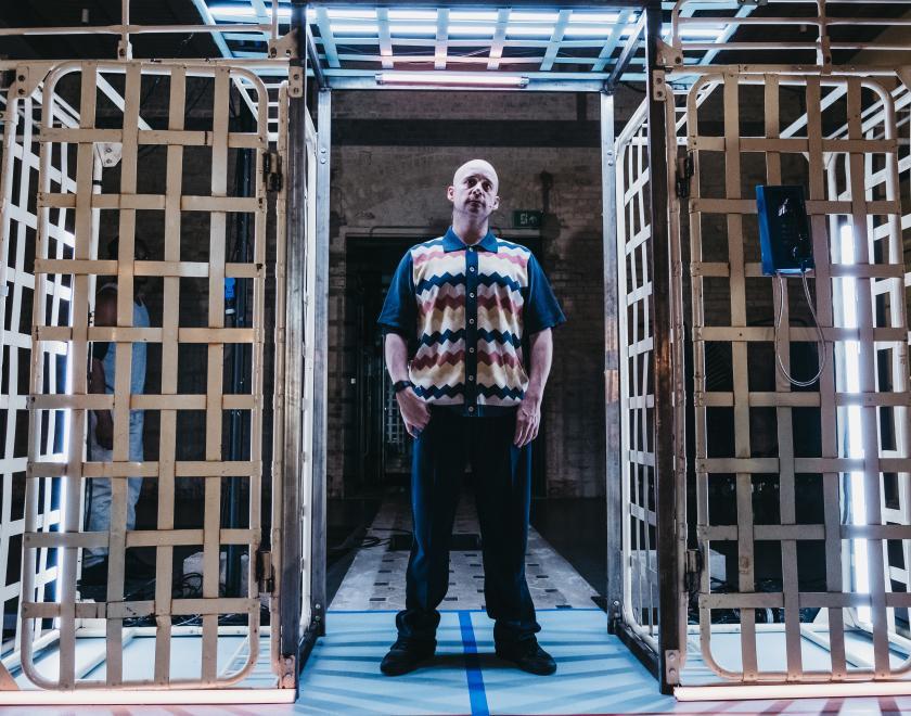 Photo of a performer standing in an archway made of prison beds.